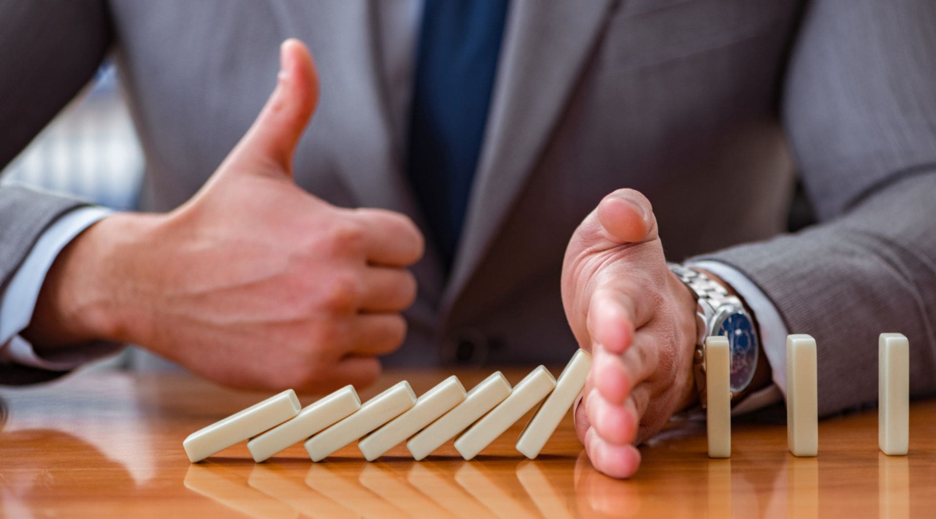 homem de terno representa o gerenciamento de crise impedindo a queda de dominós com as mãos
